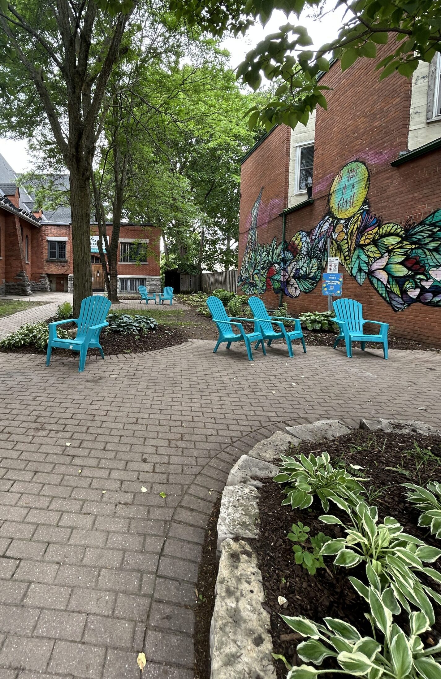 Teal Adirondack chairs in a brick courtyard beside a butterfly mural off Bank Street